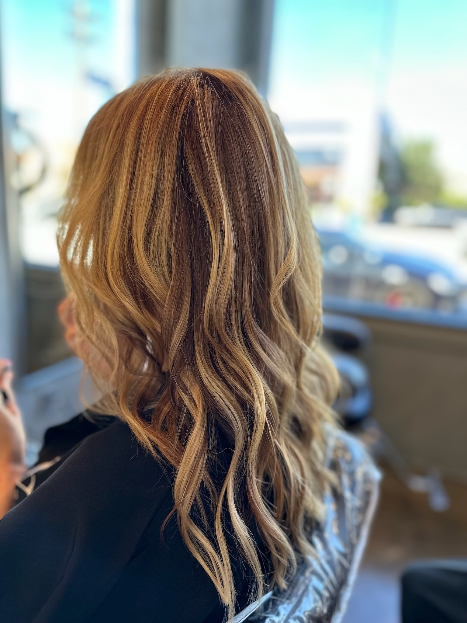 A woman with long wavy hair sits in a salon chair, preparing for a hair treatment or styling session.