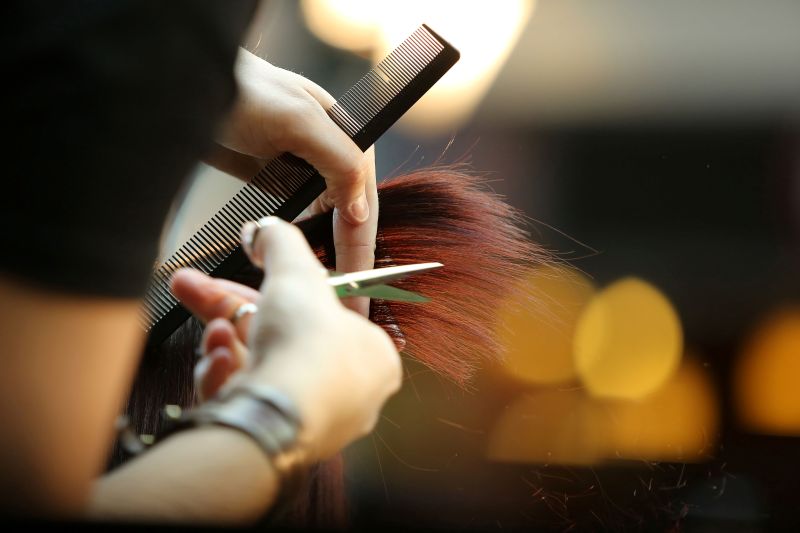 A hairstylist uses a comb to cut a woman's hair in a salon setting.