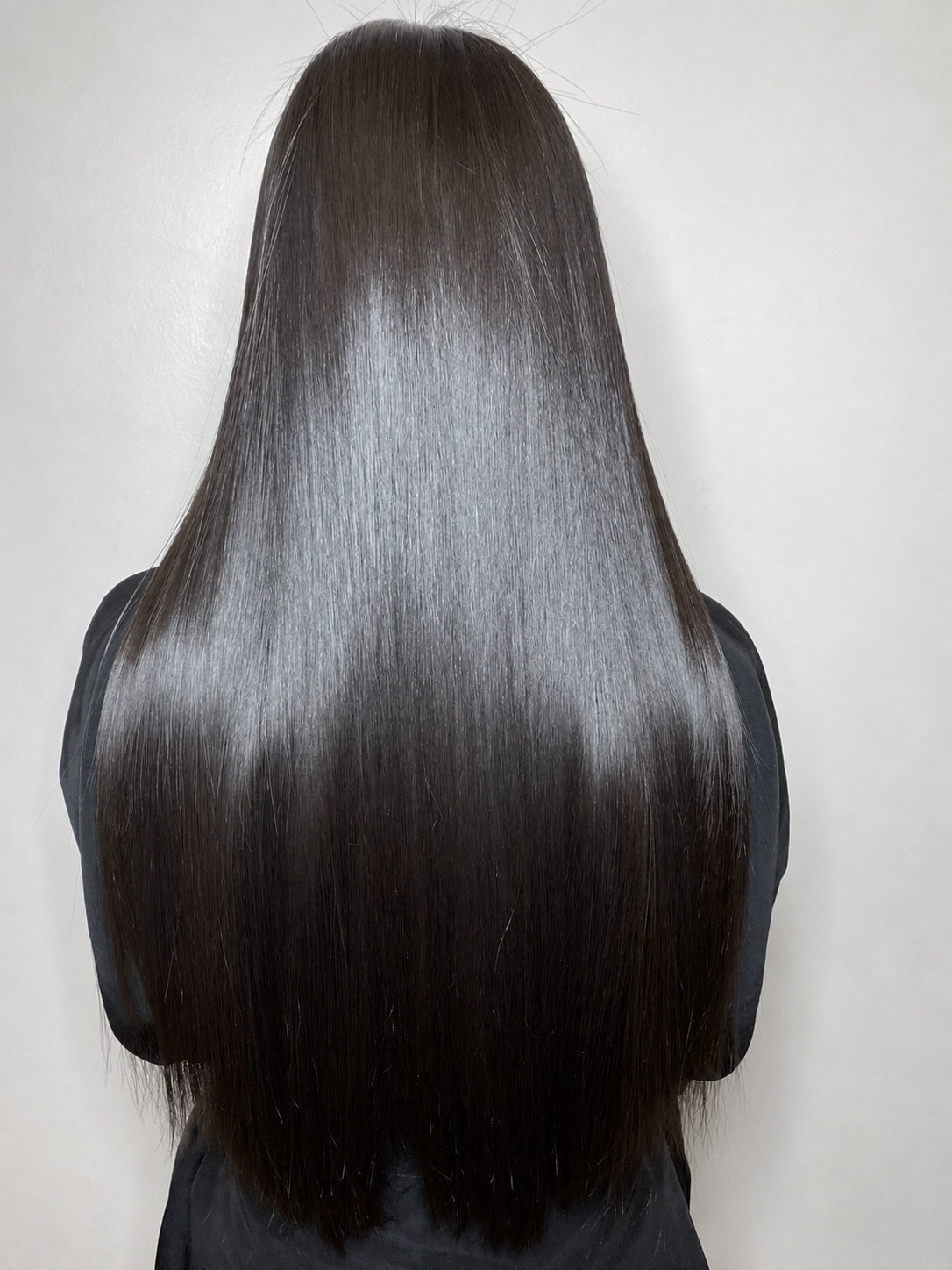 A woman's back of the head with long, straight hair cascading down her shoulders.