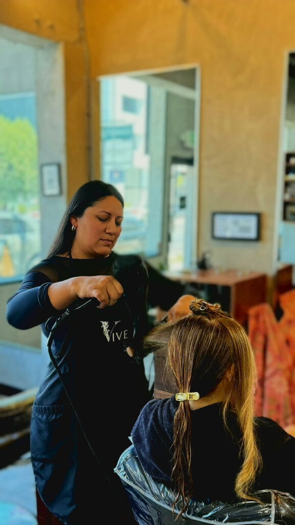 A hairstylist uses a blow dryer on wet hair in a salon. The setting features a bright, modern interior, showcasing a professional hair service.